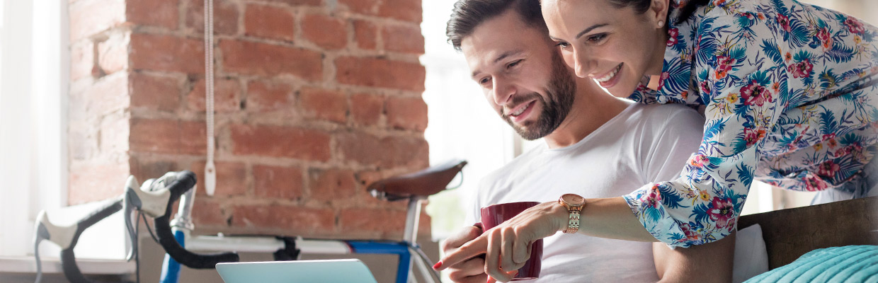 Couple drinking coffee using laptop on bed